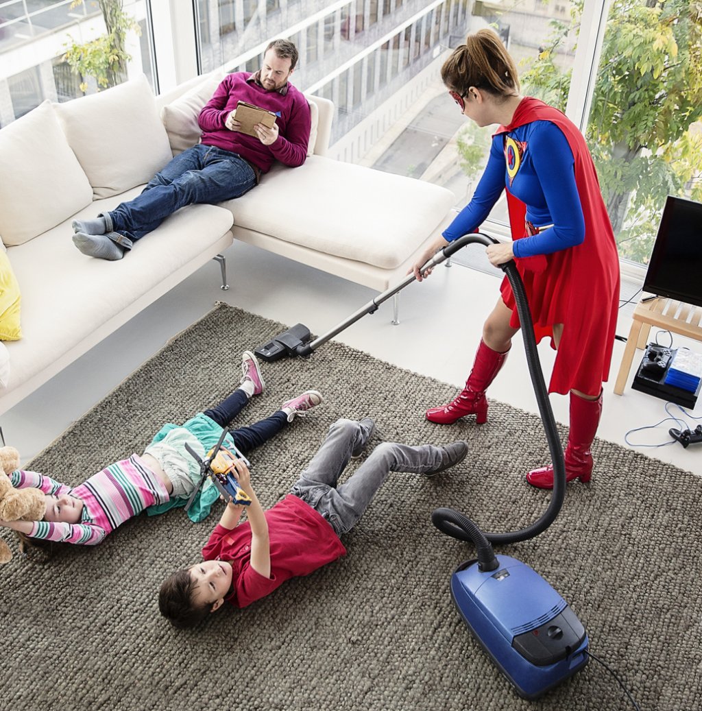 Superhero vacuuming around family in living room