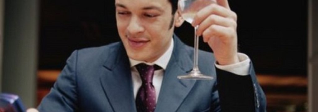 Young man at table holding wine glass and mobile phone