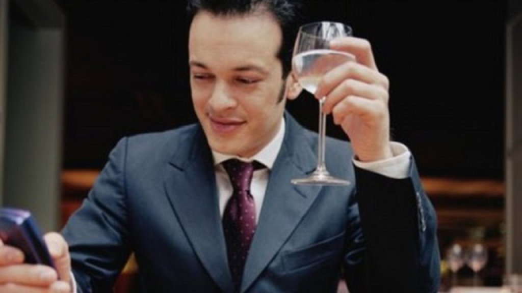 Young man at table holding wine glass and mobile phone