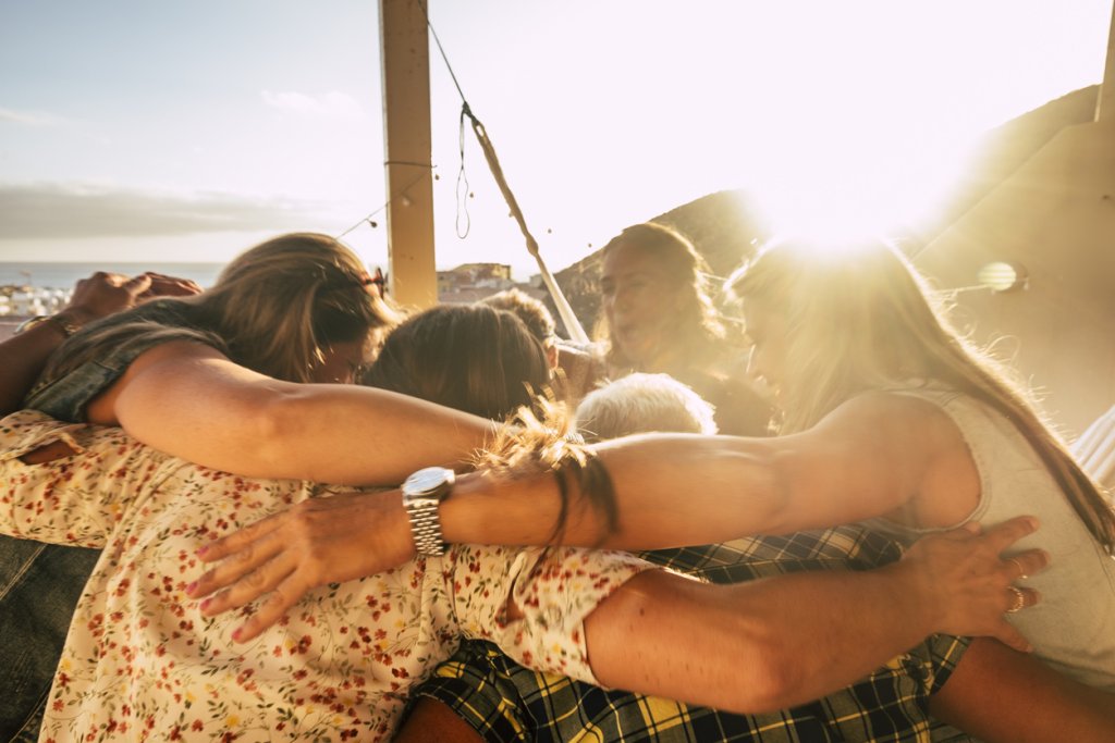 Teamwork and friendship concept for people outdoor hugging all together with love and friends lifestyle - happiness and relationship with group of females having fun - ocean view
