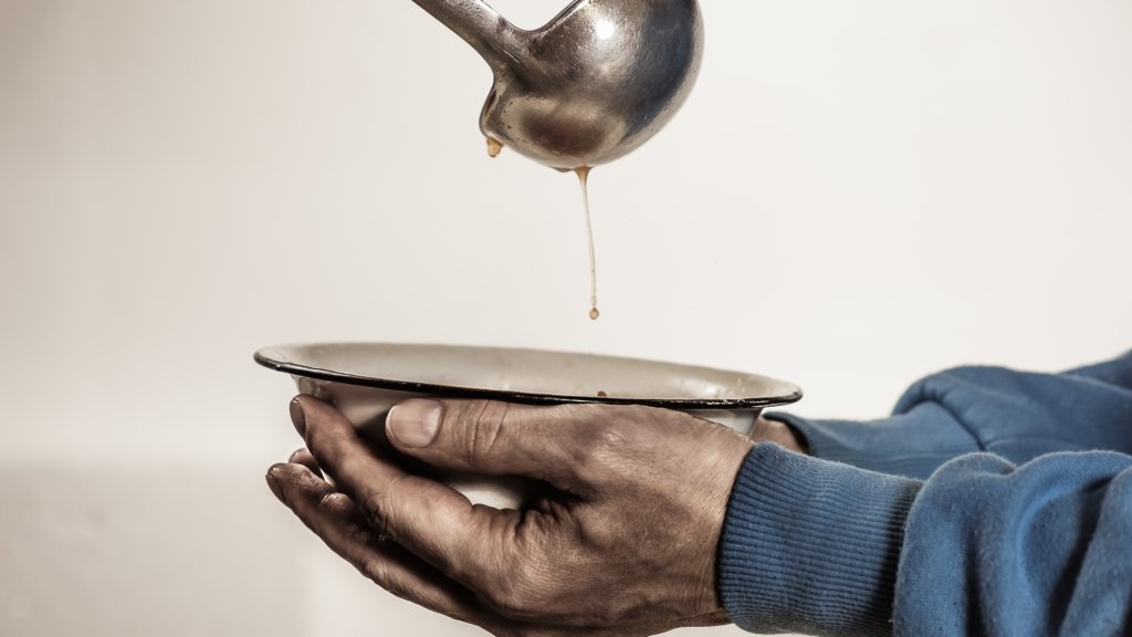 Volunteers feed the homeless. Free soup in a bowl of beggar.