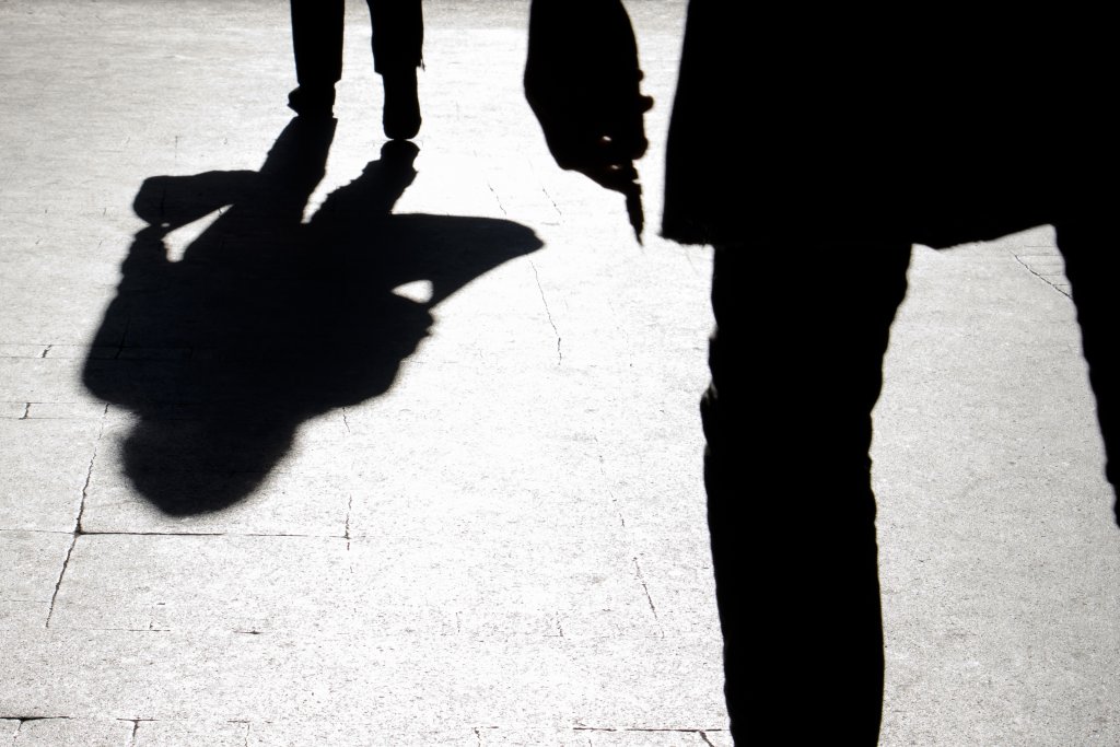 Blurry silhouette and shadow of a woman carrying a bag and a man holding sharp object following her