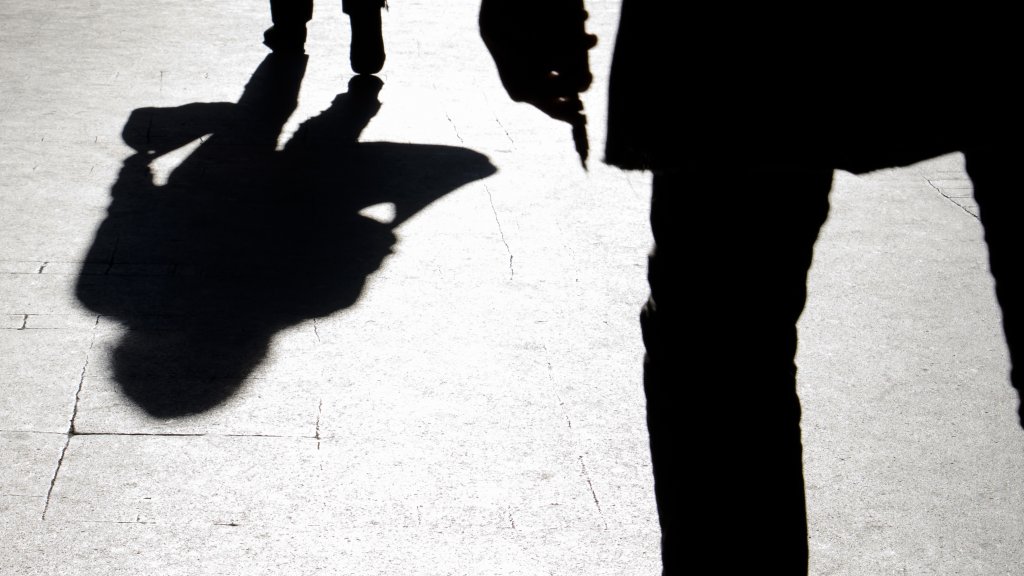 Blurry silhouette and shadow of a woman carrying a bag and a man holding sharp object following her