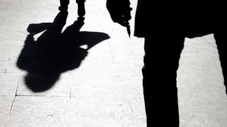 Blurry silhouette and shadow of a woman carrying a bag and a man holding sharp object following her