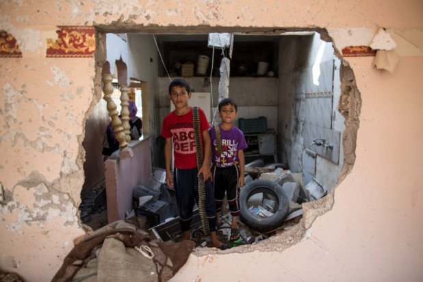 Две деца стоят в разрушения си дом и държат амуниции през август, когато 
Палестина и Израел сключиха петдневно примирие.
По време на бомбандировките загинаха 1959 палестинци.