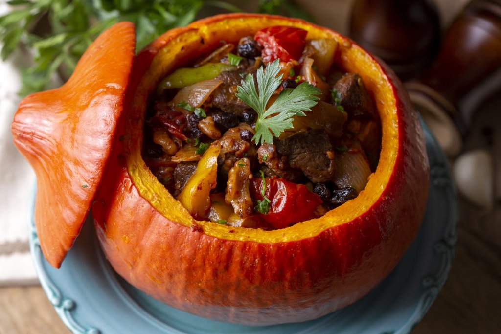 Тиква с месо и зеленчуциЗапочваме с бърза подготовка на тиквата – измиваме я старателно, махаме капачето и я издълбаваме от семките. Посоляваме, ръсим с прясно смлян черен пипер, намазняваме леко и запичаме на 180 градуса, докато омекне. През това време в голям тиган запържваме голяма глава лук и малко чесън.
Добавяме чушки на лентички и зеленчуци по избор – морков, ряпа, грах – и 500-600 грама месо по избор. Когато месото се запържи добре, слагаме щедра супена лъжица доматено пюре и чаша вода. Отново запържваме до изпаряване на водата. Пълним плънката в тиквата и печем на 180 градуса до златиста коричка.