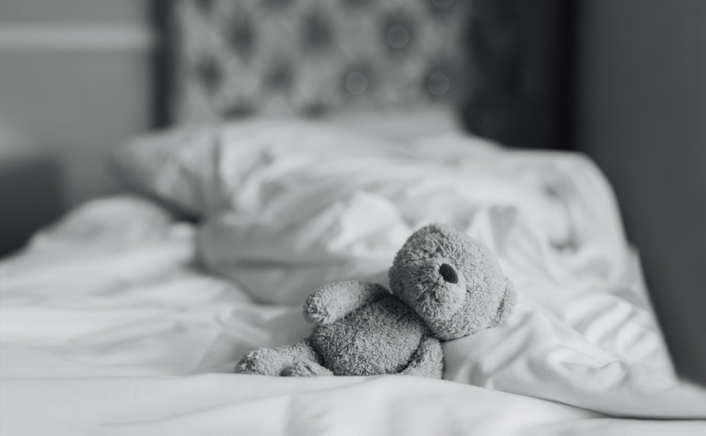 Teddy bear is lying on bed in bedroom with sunlight shining from window,Black and white photo Lonely brown bear staying alone at home, Loneliness concept, International missing Children day