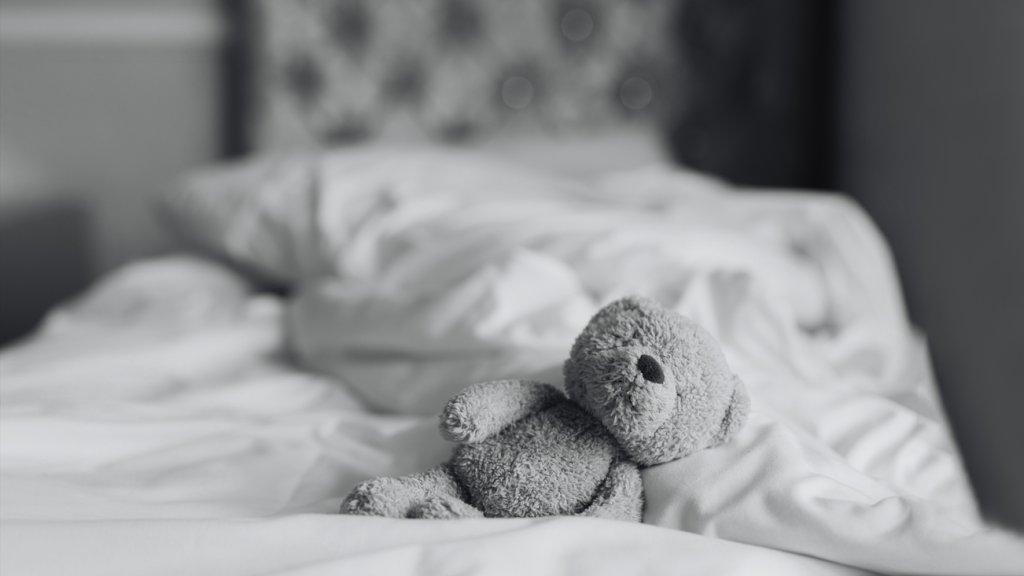 Teddy bear is lying on bed in bedroom with sunlight shining from window,Black and white photo Lonely brown bear staying alone at home, Loneliness concept, International missing Children day
