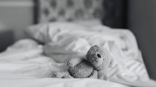 Teddy bear is lying on bed in bedroom with sunlight shining from window,Black and white photo Lonely brown bear staying alone at home, Loneliness concept, International missing Children day