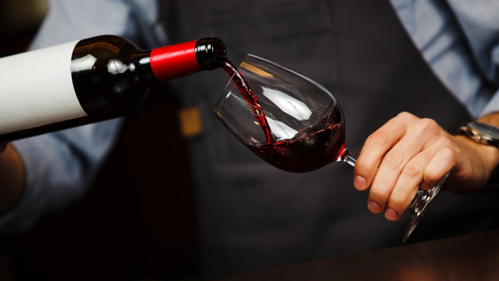Man pouring wine into wineglass, male hand holding bottle