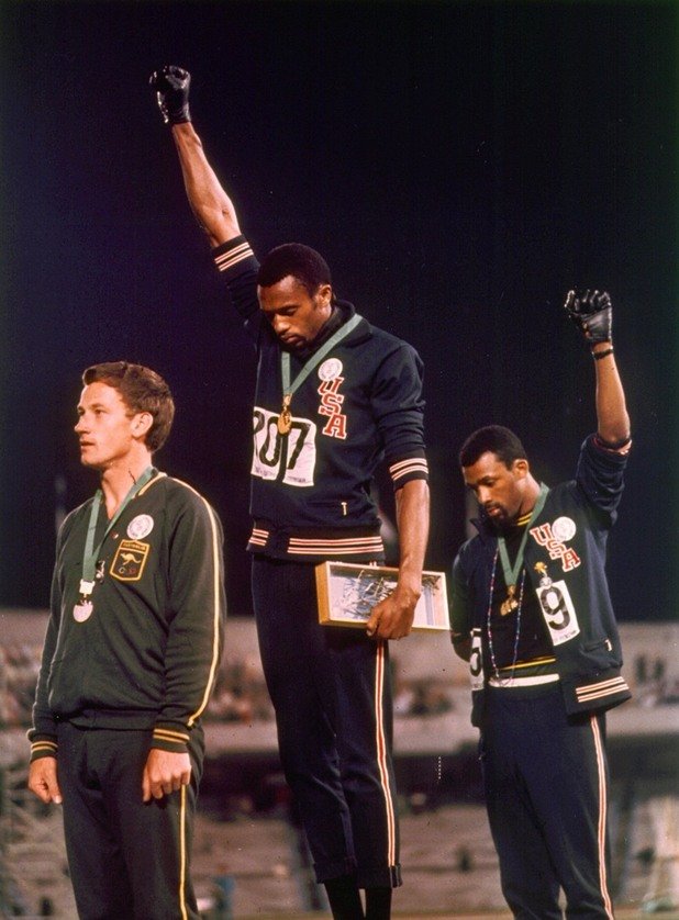 По време на Олимпийските игри през 1968-ма в Мексико Сити, фотографът Джон Доминис прави тази легендарна снимка на американските атлети Томи Cмит и Джон Карлос, които вдигат ръце по време на награждаването си. Те протестират срещу отношението на обществото към афроамериканците.
  Двамата медалисти стоят с наведени глави по време на изпълнение на американския химн. По-късно тази поза става известна като поздрава на "Черната сила" (Black Power). 
 Смит и Карлос твърдят, че в жестовете им не е имало нищо предизвикателно. Въпреки това Международният олимпийски комитет ги дисквалифицира, заради нарушаване на спортните правила чрез политическа агитация