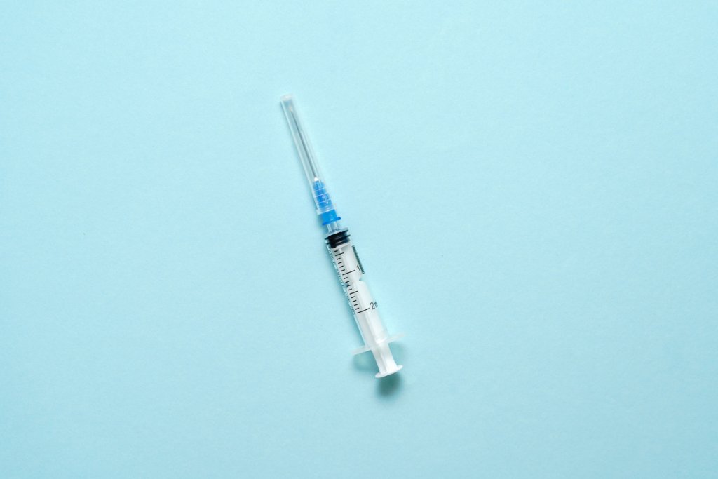 Top view of injection syringe on blue background. Minimal vaccine concept. Medical treatment of diabetes with insulin. Covid-19 vaccination. Antivax campaign