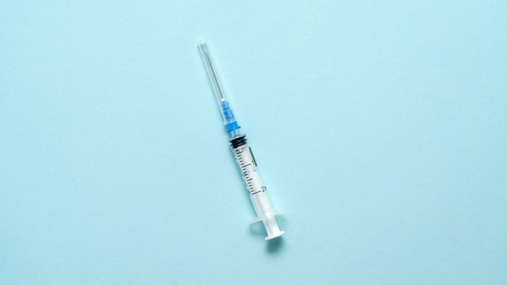 Top view of injection syringe on blue background. Minimal vaccine concept. Medical treatment of diabetes with insulin. Covid-19 vaccination. Antivax campaign