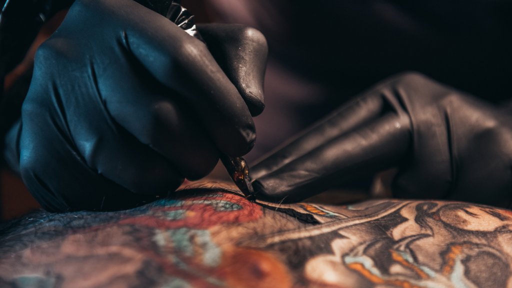 Hands of a tattoo artist wearing black gloves and holding a machine