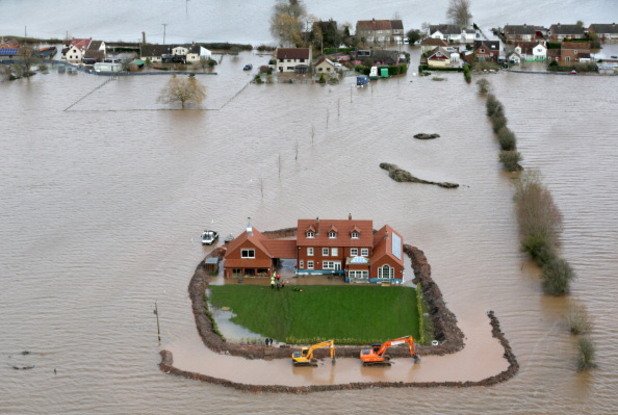 Жестоките наводнения през 2014 година нанесоха щети в много европейски държави. На снимката от  февруари работник продължава да изгражда защитни ограждения около къща в Съмърсет, Великобритания. Хиляди акри земя са потопени под водата.