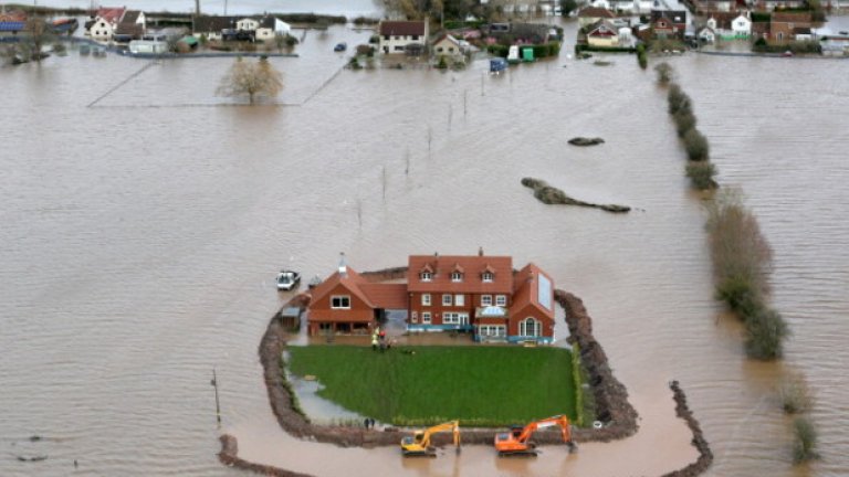 Жестоките наводнения през 2014 година нанесоха щети в много европейски държави. На снимката от  февруари работник продължава да изгражда защитни ограждения около къща в Съмърсет, Великобритания. Хиляди акри земя са потопени под водата.