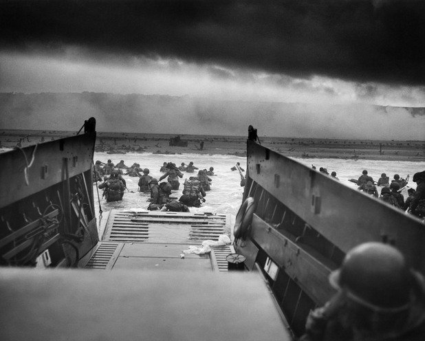 Съюзническото настъпление в Нормандия през юни 1944 година. Снимката, заснета от десантен кораб, показва как американски войници газят през студената вода до брега, където вече пристигналите военни и танк се бият с врага