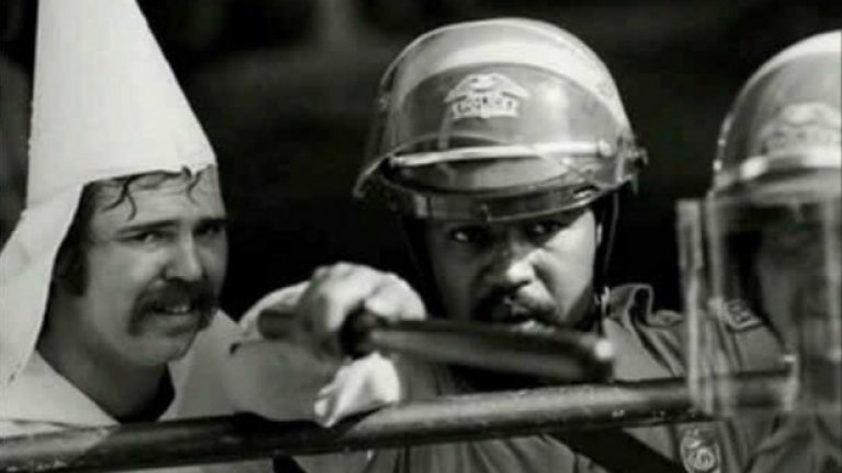Тъмнокож полицаи предпазва член на Ку Клус Клан от простестиращи, 1983 година