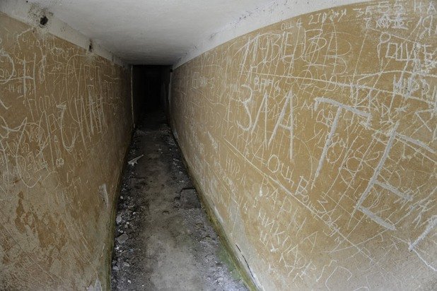 Тесен коридор отвежда към вътрешността на бункера. По стените личат надписи, оставени от отдавна служили войници
