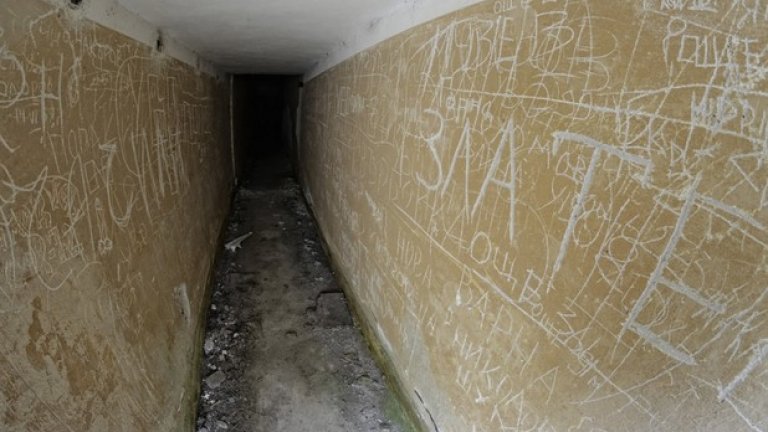 Тесен коридор отвежда към вътрешността на бункера. По стените личат надписи, оставени от отдавна служили войници