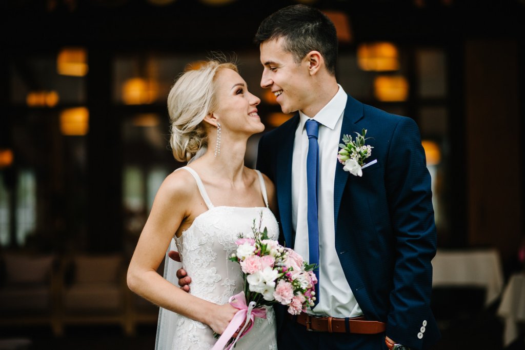 Romantic couple newlyweds, bride and groom holding bouquet of pink and purple flowers and greens with ribbon at the wedding ceremony. Happy and joyful wedding moment.