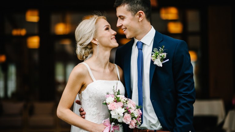 Romantic couple newlyweds, bride and groom holding bouquet of pink and purple flowers and greens with ribbon at the wedding ceremony. Happy and joyful wedding moment.