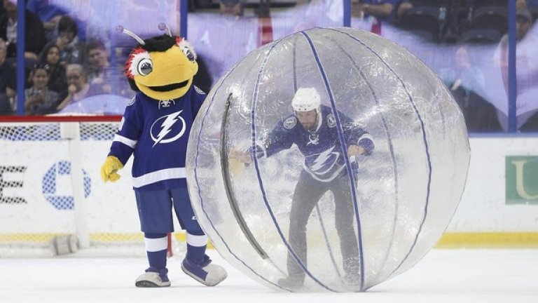 Тъндър Бъг, талисманът на Тампа в НХЛ, помага на фен в опита му да издържи на играта "човека-хамстер", популярна и из софийските паркове. Само че тук е на лед...
