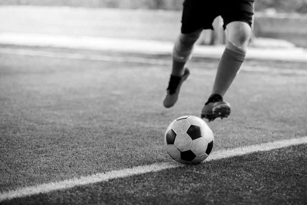 black and white image of the soccer player shoot ball on artificial turf.