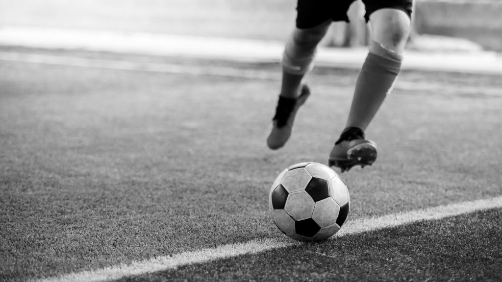 black and white image of the soccer player shoot ball on artificial turf.