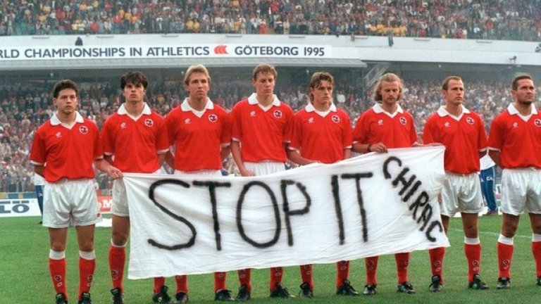 5. Възходът през 90-те
Прогресът в модерния швейцарски футбол тръгва в началото на 90-те години. Тогава за селекционер на националния отбор е нает Ули Щилике. Под негово ръководство е постигната историческата победа над България с 3:2 в София на 1 май 1991 г., когато нападателят с турски корени Кубилай Туркилмаз носи триумфа с гол в последната минута, а Швейцария завършва само на точка от участие на Евро `92. Англичанинът Рой Ходжсън наследява Щилике и класира състава на световното в САЩ `94. Последният мач от квалификациите срещу Естония (4:0) се играе пред федералните канцлери Рут Дрейфюс и Адаолф Оги, а тв-аудиторията надхвърля 2 милиона зрители. На световното Швейцария достига осминафинал, където губи от Испания на дузпи. След това успява да влезе и сред 16-те финалисти на Евро `96, а квалификационният мач срещу Швеция в Гьотеборг остава в историята с плаката „Stop it Chirac”, издигнат от швейцарските футболисти (на снимката) срещу намеренията на френския президент Жак Ширак за извършване на ядрени опити. На европейското воденият от португалеца Артур Жорже състав не успява да прескочи групите. Но възходът в швейцарския футбол вече е очевиден.