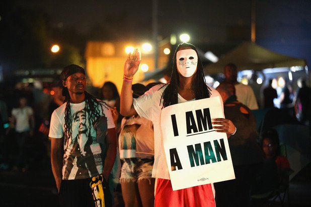 Жена протестира с бяла маска на лицето и плакат, на който пише "Аз съм мъж" 