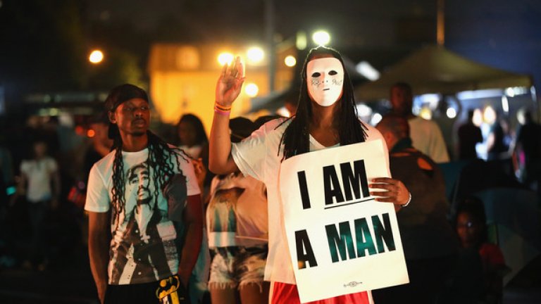 Жена протестира с бяла маска на лицето и плакат, на който пише "Аз съм мъж" 