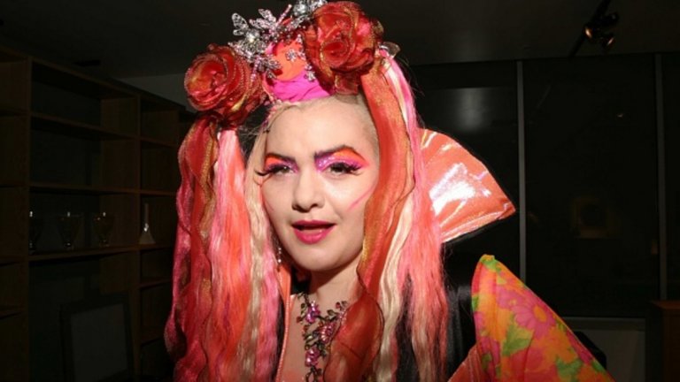Тя е с впечатляваща розова перука, тежък грим, огромно деколте. Казва се Ейнджъл Айдиализъм и е най-известната астроложка в Ню Йорк.