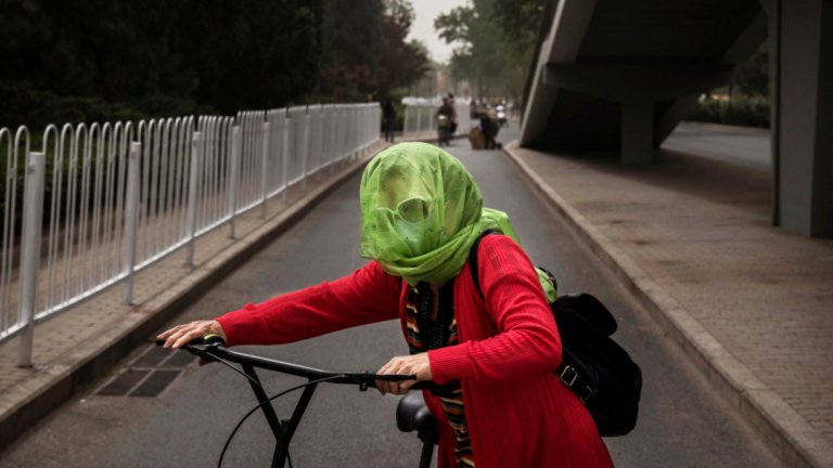 Жена се крие с шала си от силния вятър и пясъчните частици