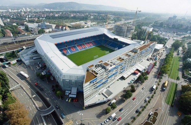 8. Футболната арена „Санкт Якоб”

Ако в Швейцария най-митичният стадион е „Ванкдорф” в Берн, където през 1954 г. се играе финалът на световното между ФРГ и Унгария (3:2), днес „Санкт Якоб” в Базел се явява нещо като сърцето на футбола в страната. Арена не само за местния шампионски тим, но и на националния отбор. 40-хилядното съоръжение е построено между 1999 и 2001 г. срещу инвестиция от 220 милиона швейцарски франка, отдавна покрити от таксите на триетажния търговски център „Манор”, вграден в трибуните. Нещо повече – в едната от фасадите на „Санкт Якоб” има не само офиси, но и апартаменти, в които живеят инвалиди. По законите в страната това води до данъчни облекчения за търговското дружество „Базел Юнайтед”, което е собственик на стадиона. Хитро измислено!
Над 600 000 души посещават стадиона и търговския център всяка година, което осигурява около 70% от приходите на футболния клуб. На „Санкт Якоб” се провежда и откриването на Евро 2008, чието домакинство бе поверено на Швейцария и Австрия. На същото първенство управата на стадиона осъществи безпрецедентна акция по смяна на терена, който бе станал на парцали заради проливния дъжд на мача Швейцария – Турция (1:2). Новите чимове бяха поръчани от Холандия още на полувремето, след като се видя, че игрището загива. 26 камиона потеглиха веднага към Базел, а само за 24 часа работа цялата трева беше подменена с нова.