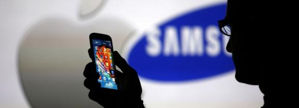 A man is silhouetted against a video screen with Apple and Samsung logos as he poses with a Samsung Galaxy S4 in this photo illustration taken in the central Bosnian town of Zenica