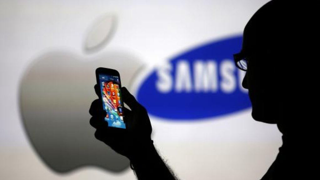 A man is silhouetted against a video screen with Apple and Samsung logos as he poses with a Samsung Galaxy S4 in this photo illustration taken in the central Bosnian town of Zenica