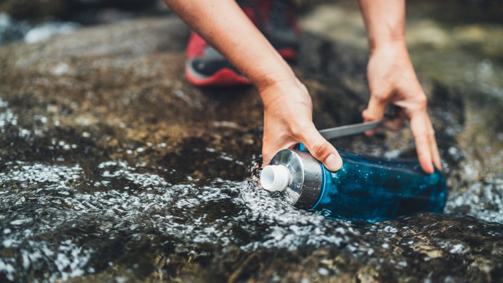 Close-up photo of female hands filling up a fresh cold mountain stream water into the plastic touristic bottle while water break on the tourist hiking route. Active people or water resources concept.