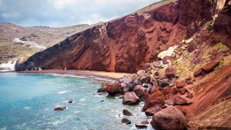 Остров СанториниНедалеч от Акротири е един от най-популярните и атрактивни плажове на Санторини – Червеният плаж. На него червеният пясък е примесен с малки червени камъчета, а скалите над плажа са в интересни нюанси. Ако обичате гмуркането – Червеният плаж може да ви предложи причудливи подводни пейзажи. Санторини има и Черен и Бял плаж, до които се стига с лодка от Акритори. Името им отново идва от цвета на пясъка и камъчетата по бреговата ивица.
До Санторини можете да стигнете със самолет, но към момента няма директни полети от Летище София. Ще ви се наложи да се прикачите в Атина или в Солун. Летището се намира северно от селището Камари. Оттам лесно можете да стигнете до град Фира, а от Фира и до другите части на острова. Ако решите да пътувате с автомобил, можете да хванете ферибот от пристанищата на Солун, Пирея до Атина или Крит. Пътуването отнема от 5 до 9 часа в зависимост от междинните спирания.
