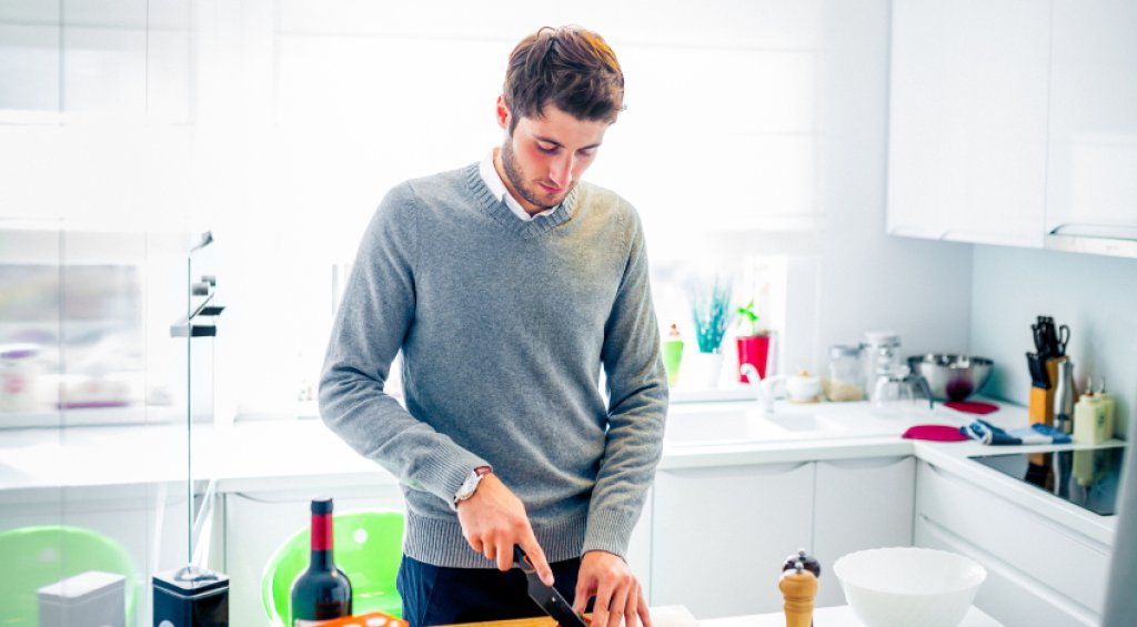 Handsome young man cooking at home cutting vegetables