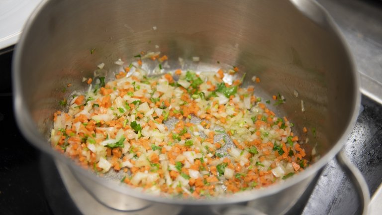 4. Загравяме голяма тенджера с дебело дъно на среден огън.

Добавяме олио или зехтин, малко масло и слагаме лука, морковите, целината, чесъна (цял, необелен), мащерката и дръжките на магданоза, нарязани на ситно.
Запържваме около 15 минути на нисък пламък, за да може морковите да пуснат цвета си.
Chefs Tip: За по-интересен вкус на този етап може да сложите малко куркума, шафран или къри, както и малко лимонова кора.