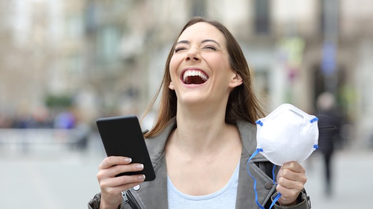 Excited woman holding phone and mask on a street