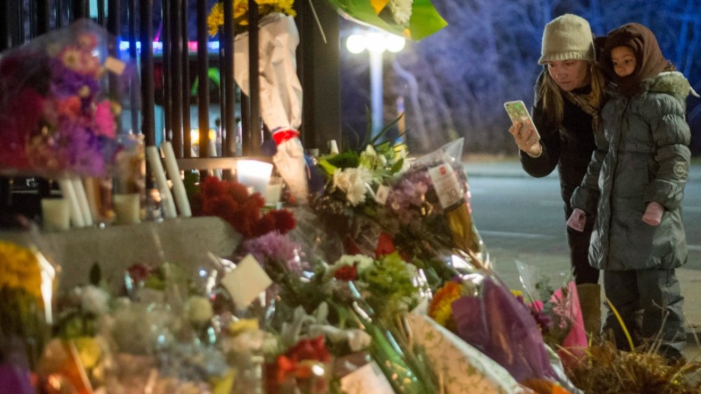 a-mother-and-child-take-photographs-of-a-memorial-with-flowers-and-candles-at-the-gates-of-the-embas