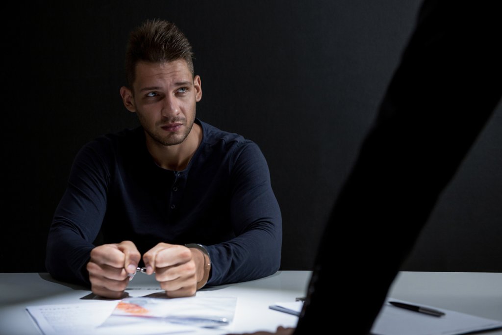 Criminal man with handcuffs in interrogation room