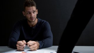 Criminal man with handcuffs in interrogation room