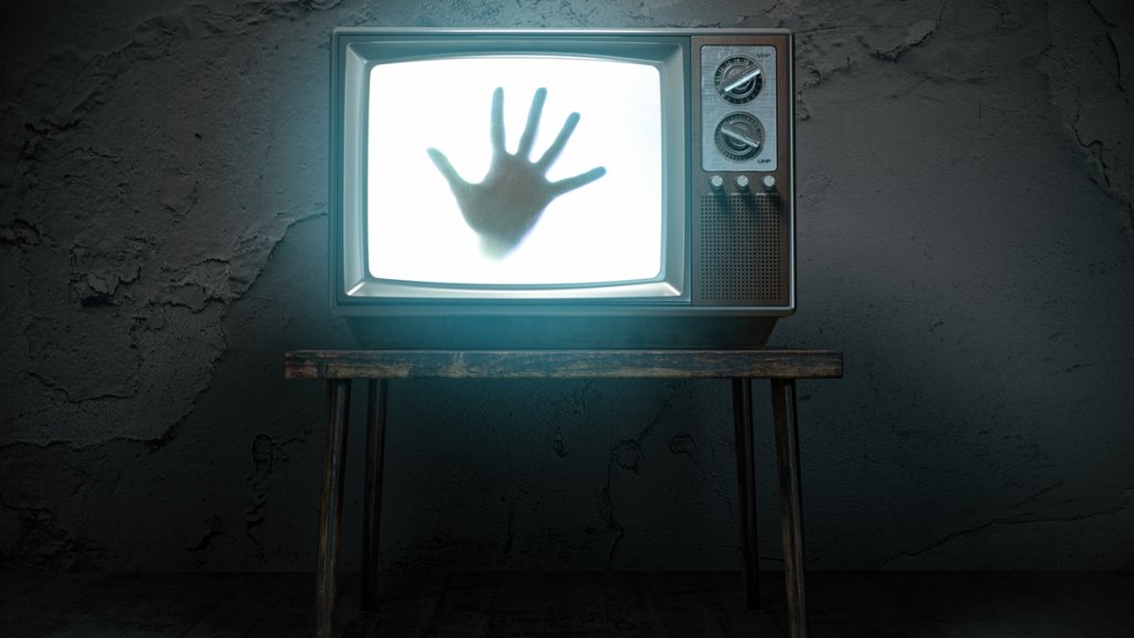 Horror scary movie concept. Hand of ghost on screen of vintage tv in haunted house.