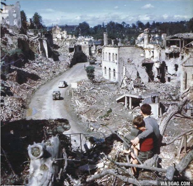 Две деца гледат как американски войници влизат в разрушен град във Франция след десанта в Нормандия през Втората световна война