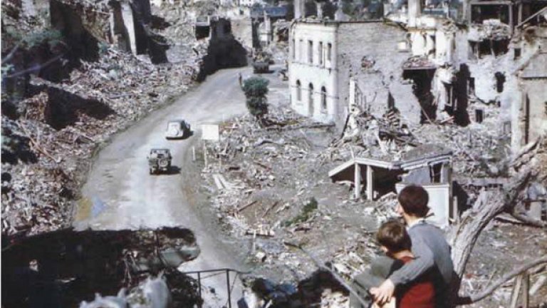Две деца гледат как американски войници влизат в разрушен град във Франция след десанта в Нормандия през Втората световна война