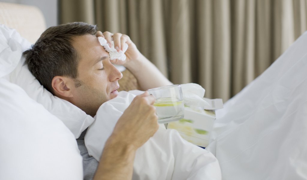 Man sick in bed drinking hot drink