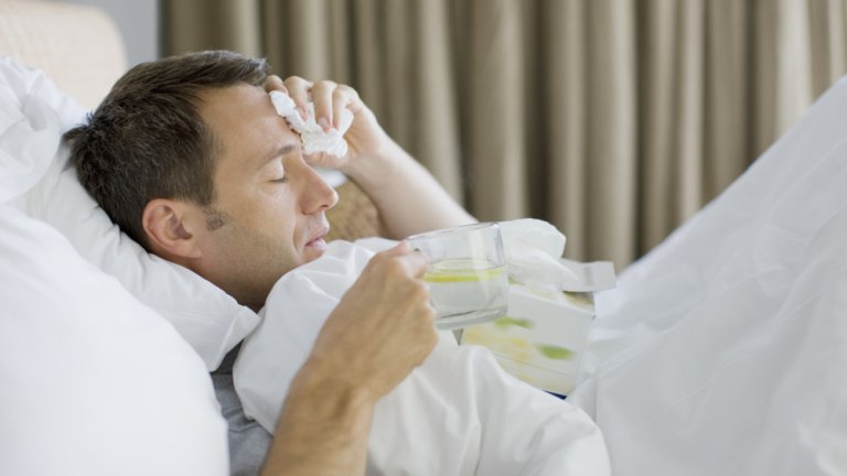 Man sick in bed drinking hot drink